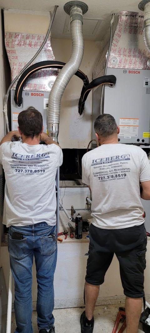 Two people in white shirts working on HVAC equipment indoors.