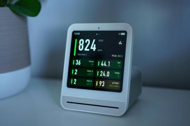 White air quality monitor displaying numerical data on a white shelf.