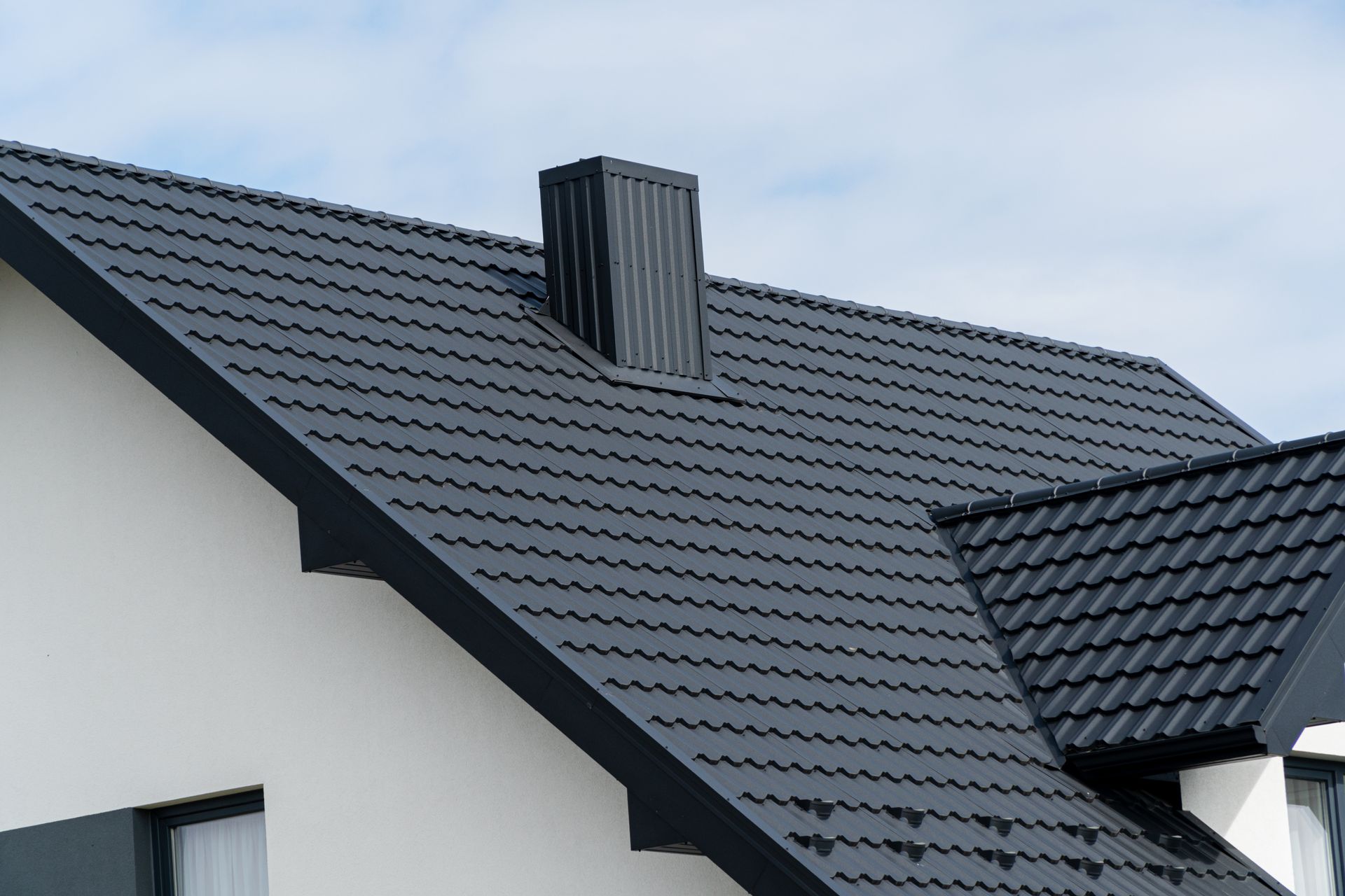 A white house with a black roof and a chimney on the roof.