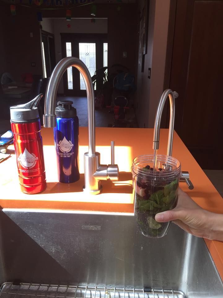 Person filling a glass with water over a sink, with two water bottles on counter.