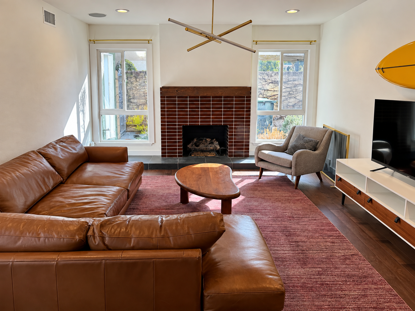 Cozy living room with brown leather sectional, red rug, brick fireplace, and TV console