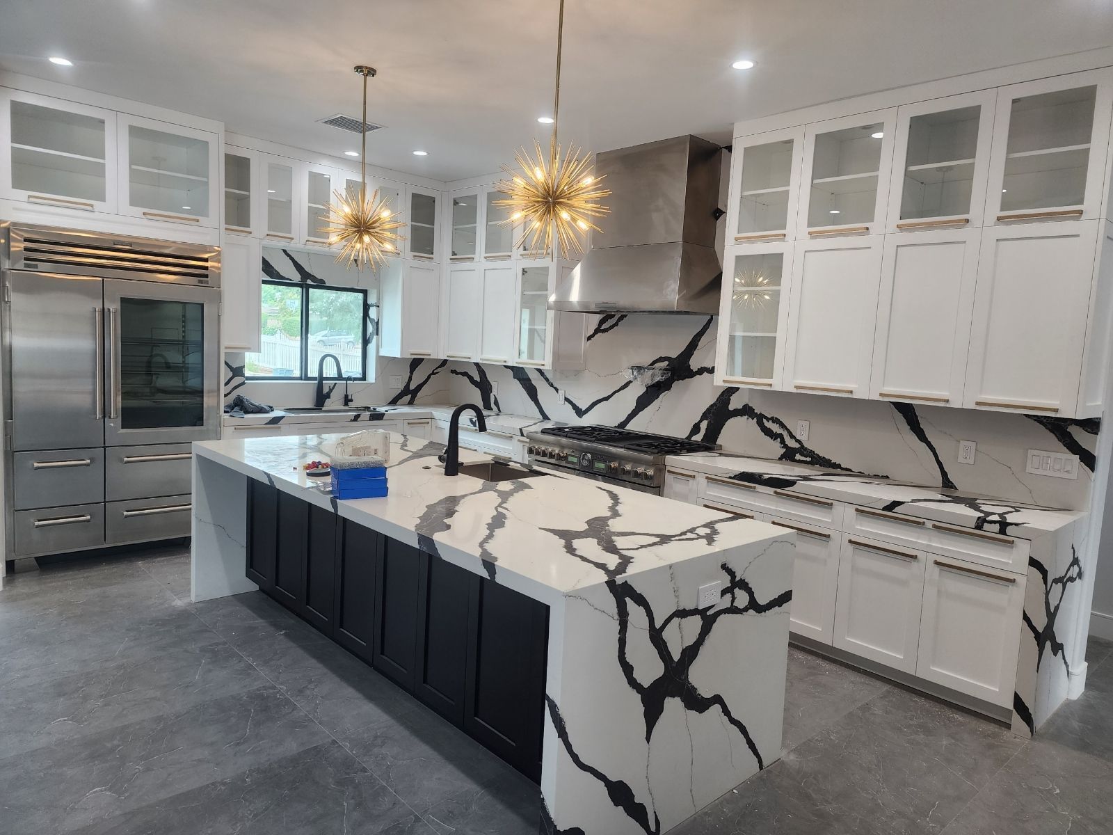 Modern white kitchen with black-veined marble island, pendant lights, and stainless steel appliances