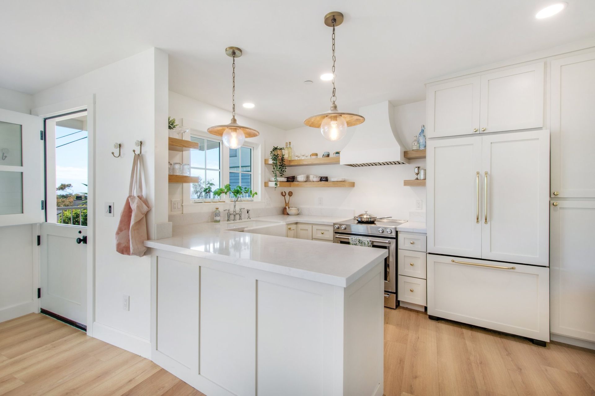 Bright white kitchen with island, pendant lights, farmhouse sink, and stainless steel refrigerator