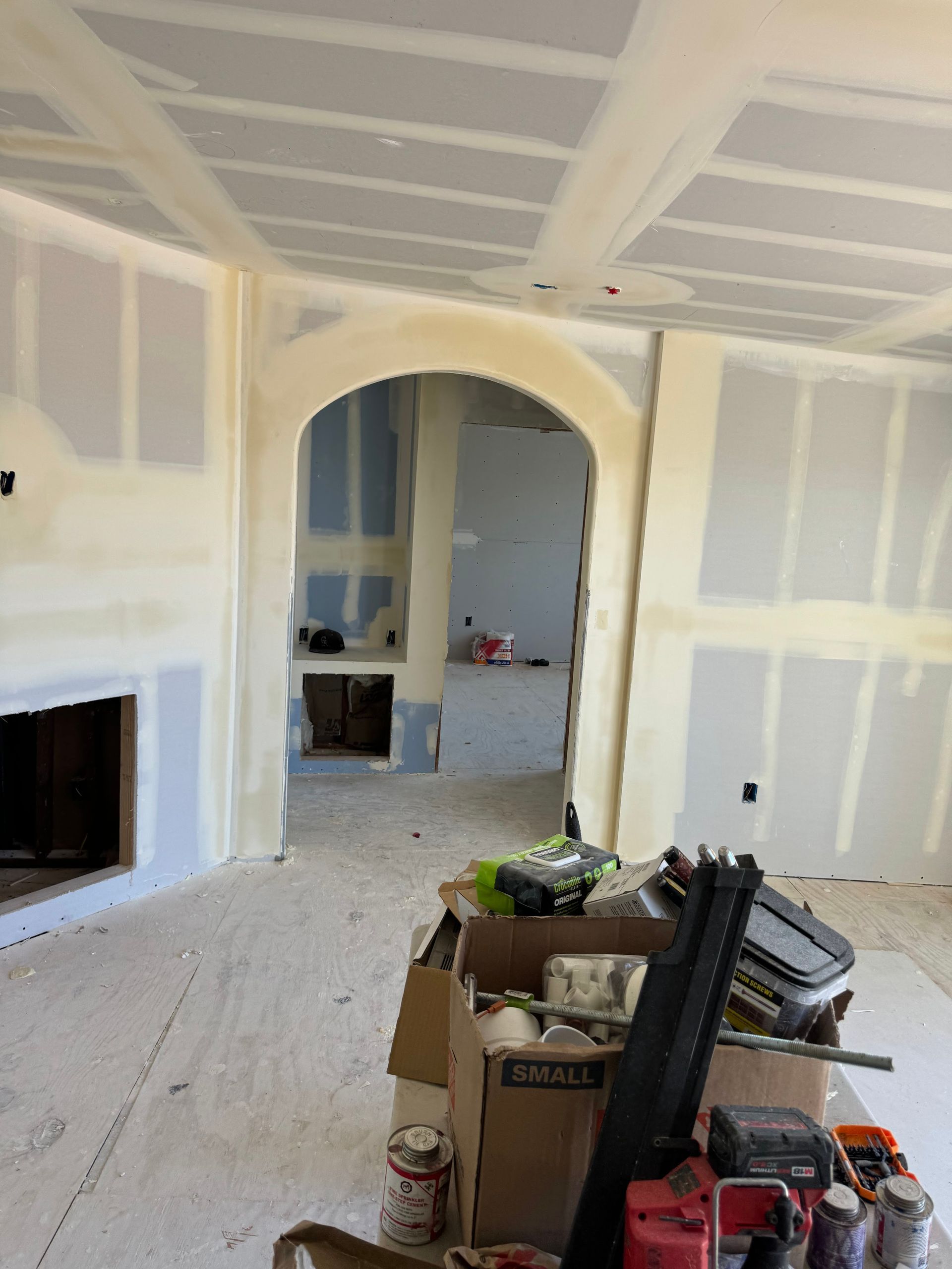 Unfinished room with drywall, arched doorway, fireplace, and construction materials on the floor.