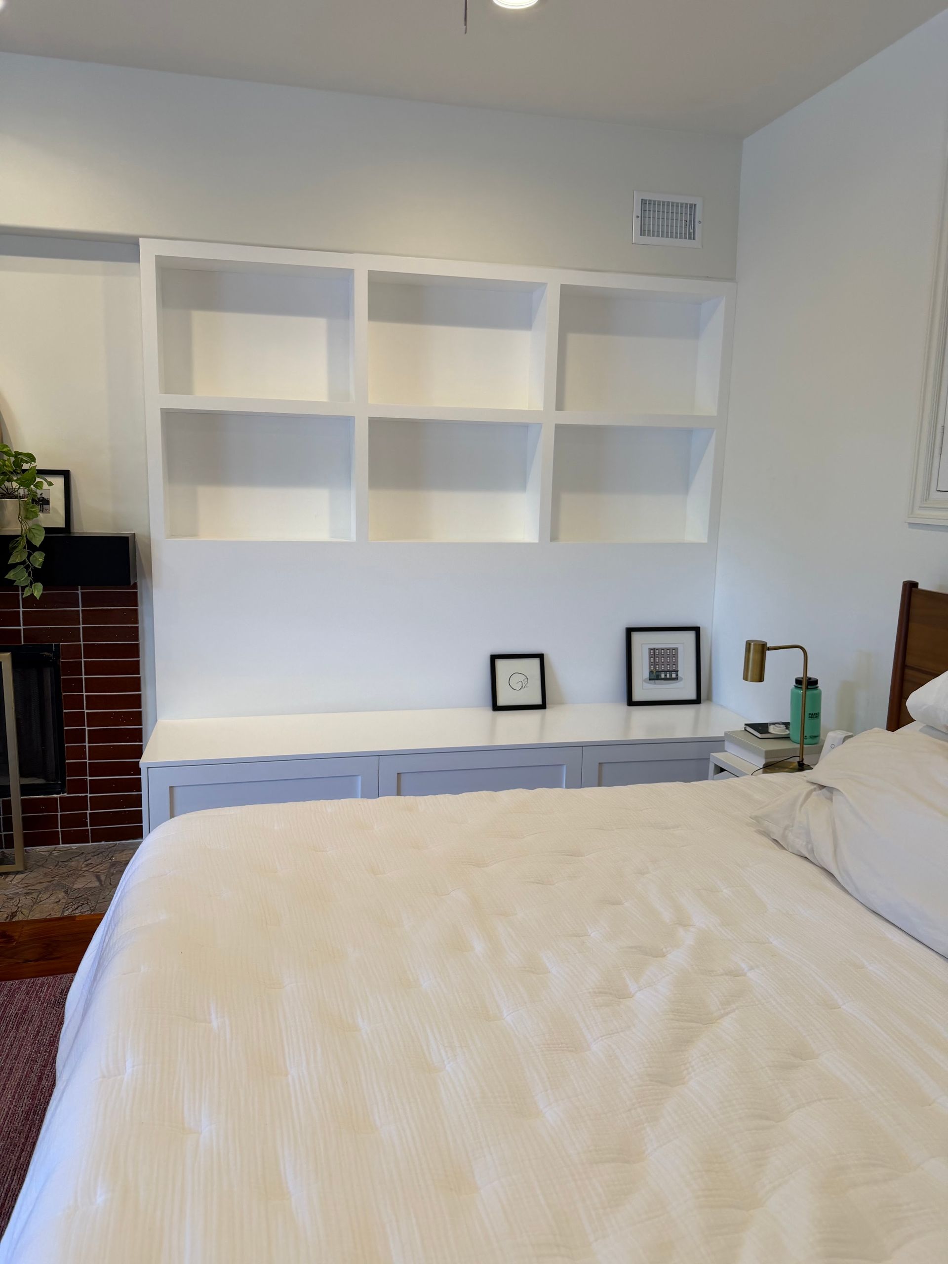 Bedroom with white shelving, dresser, and a bed with a cream blanket and pillows