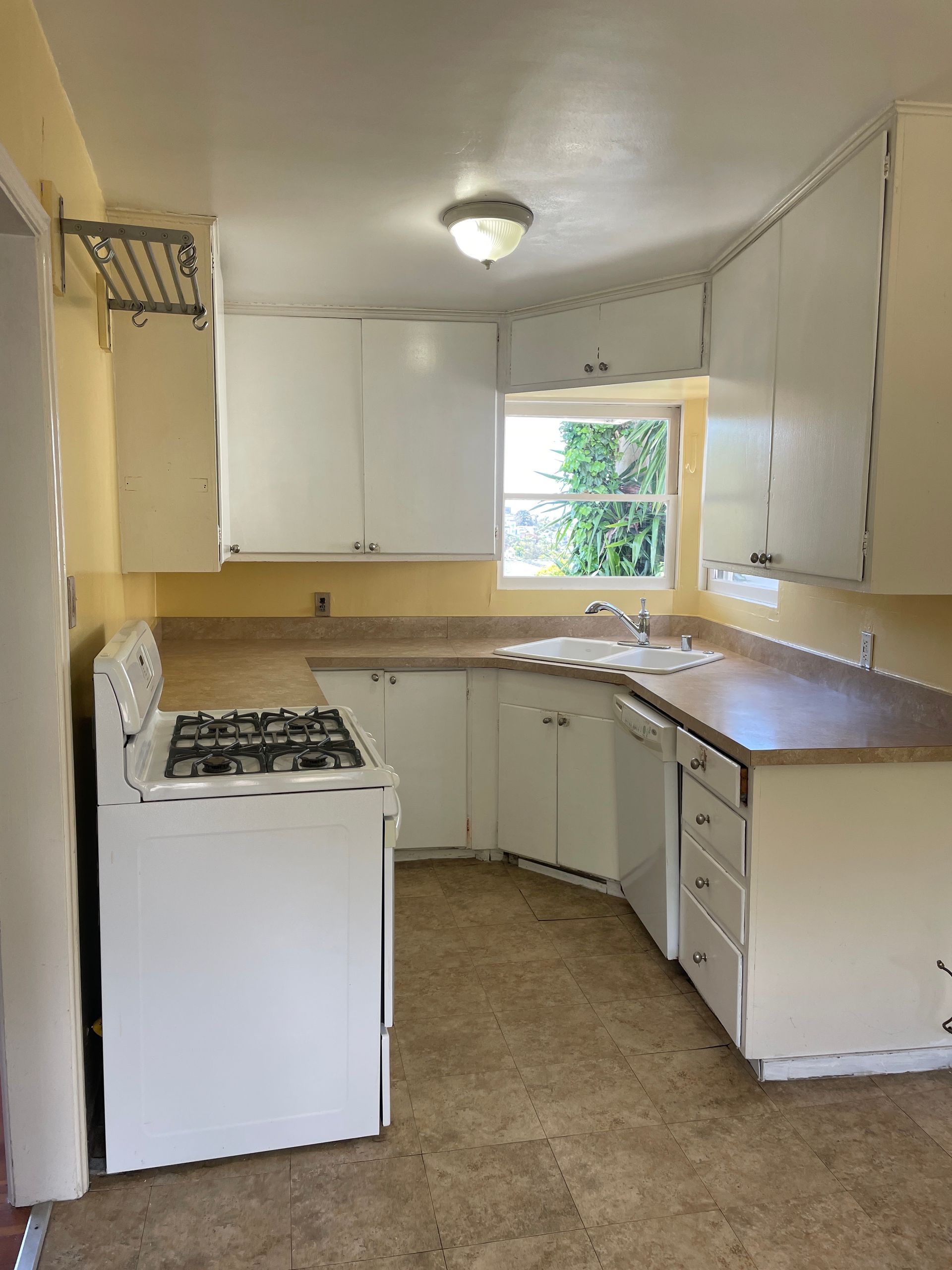 Small kitchen with white cabinets, gas stove, brown counters, and a window over the sink.