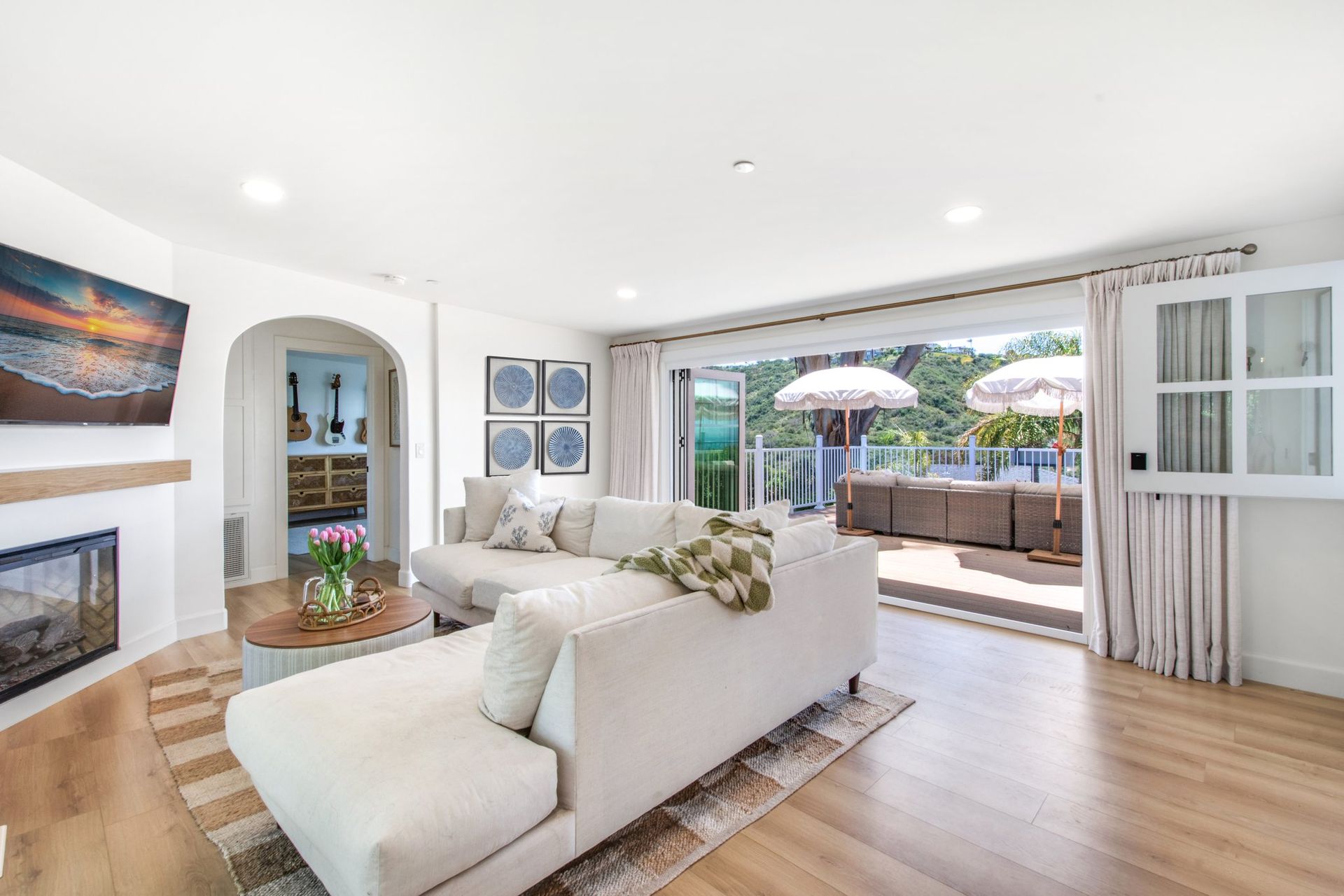 Bright living room with white sofa, wood floors, fireplace, and open doors to a sunny patio