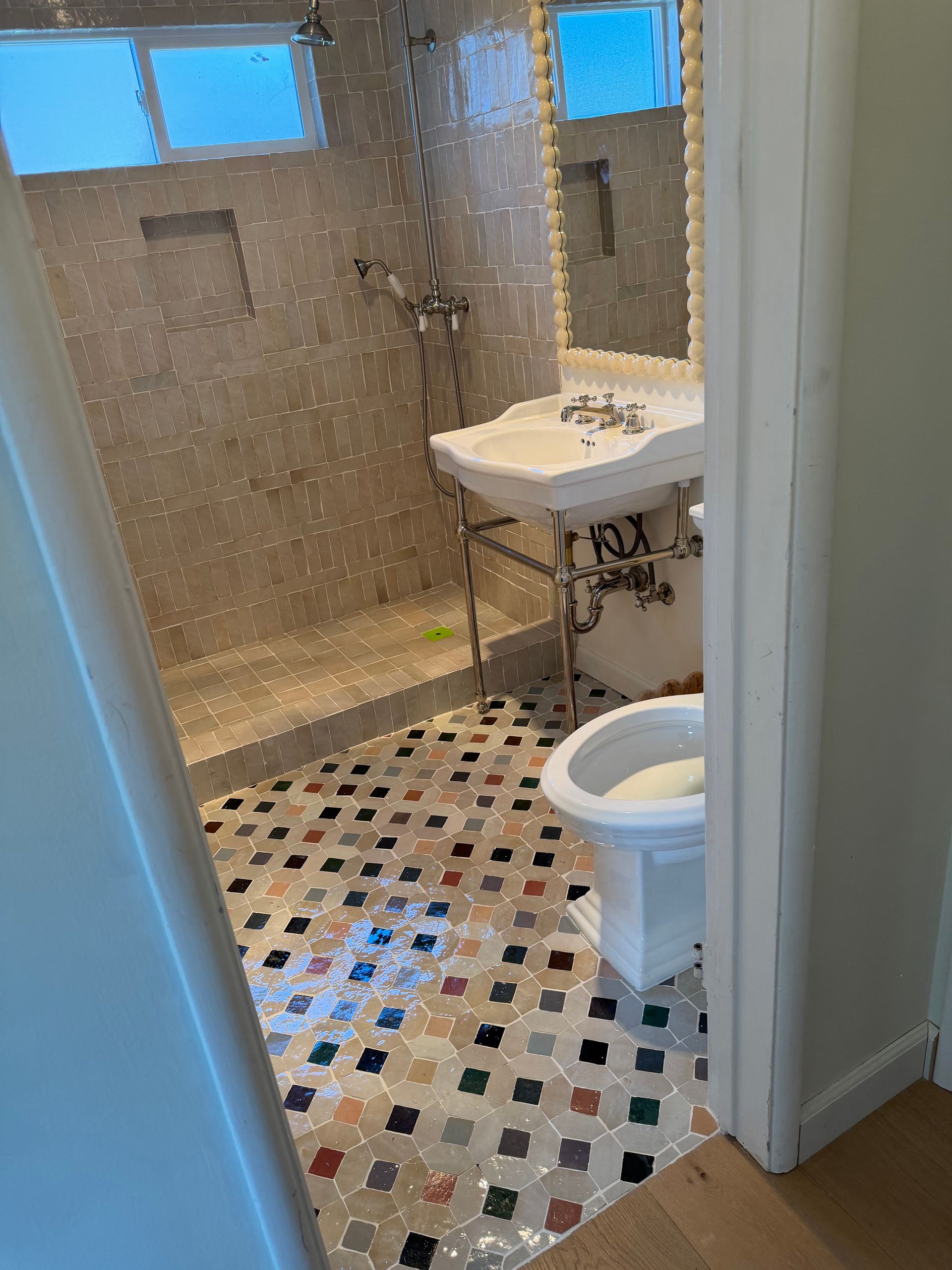Small tiled bathroom with a sink, toilet, and shower stall visible through a doorway.