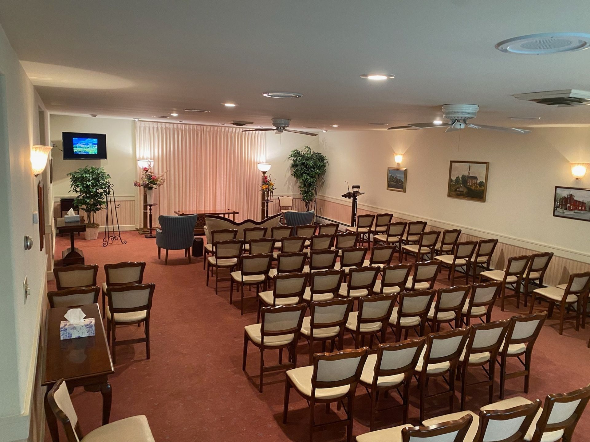 Empty meeting room with rows of chairs facing a small screen and stage area