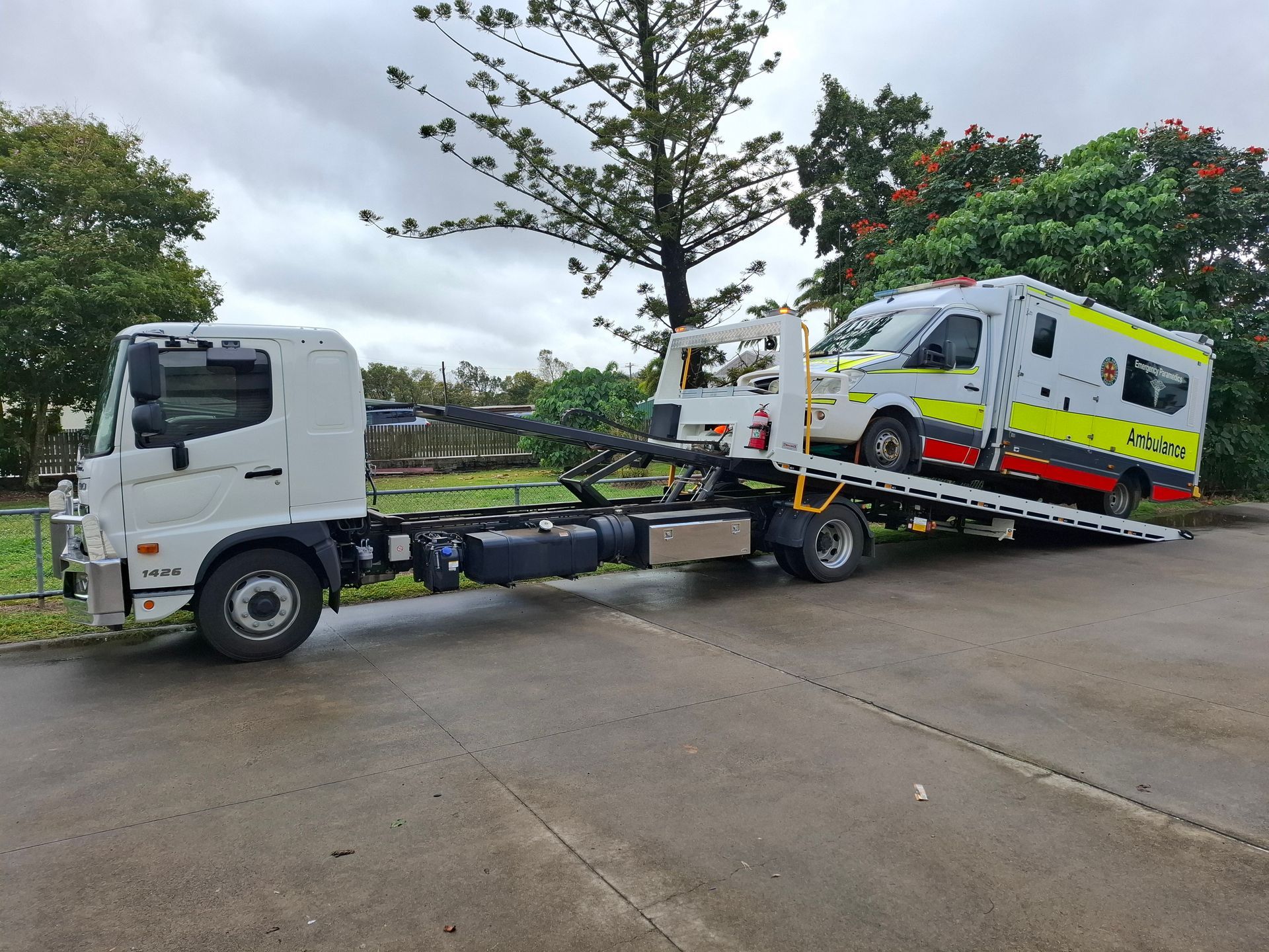 Tow Truck Loading a White Ambulance on a Flatbed Ramp in a Roadside Lot — Airlie Towing & Tilt Tray Hire In Cannonvale, QLD