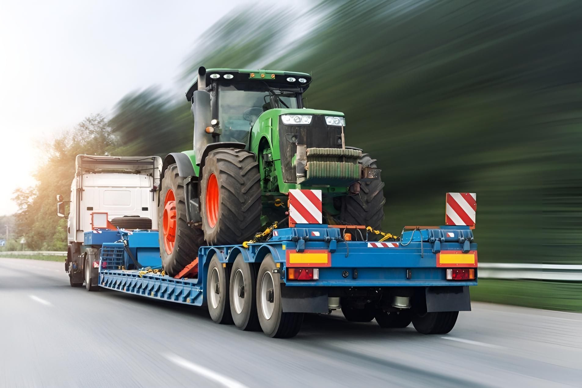 A Tractor is Being Transported on a Trailer on a Highway — Airlie Towing & Tilt Tray Hire In  Airlie Beach, QLD