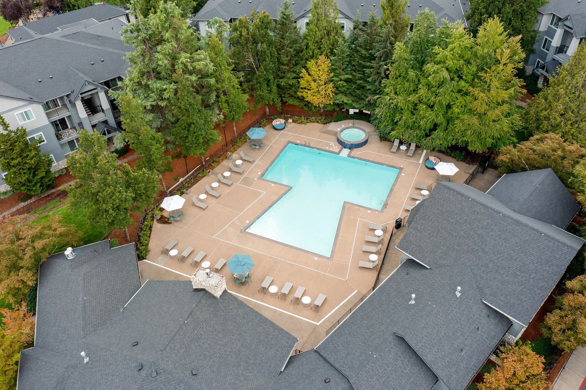 Aerial view of apartment community pool with lounge chairs and a hot tub, surrounded by trees.
