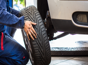 Mechanic checking a car tire next to a white vehicle in a garage | Zee's Alignment & Autocare