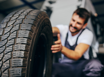 Mechanic inspecting a car tire in a garage, with a tread pattern in the foreground | Zee's Alignment & Autocare