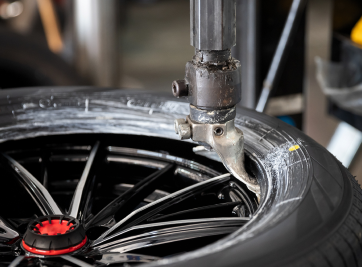Tire-changing machine removing a black car tire from a shiny alloy wheel in a workshop | Zee's Alignment & Autocare