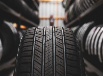 Close-up of a car tire in a tire shop aisle with rows of tires blurred in the background | Zee's Alignment & Autocare