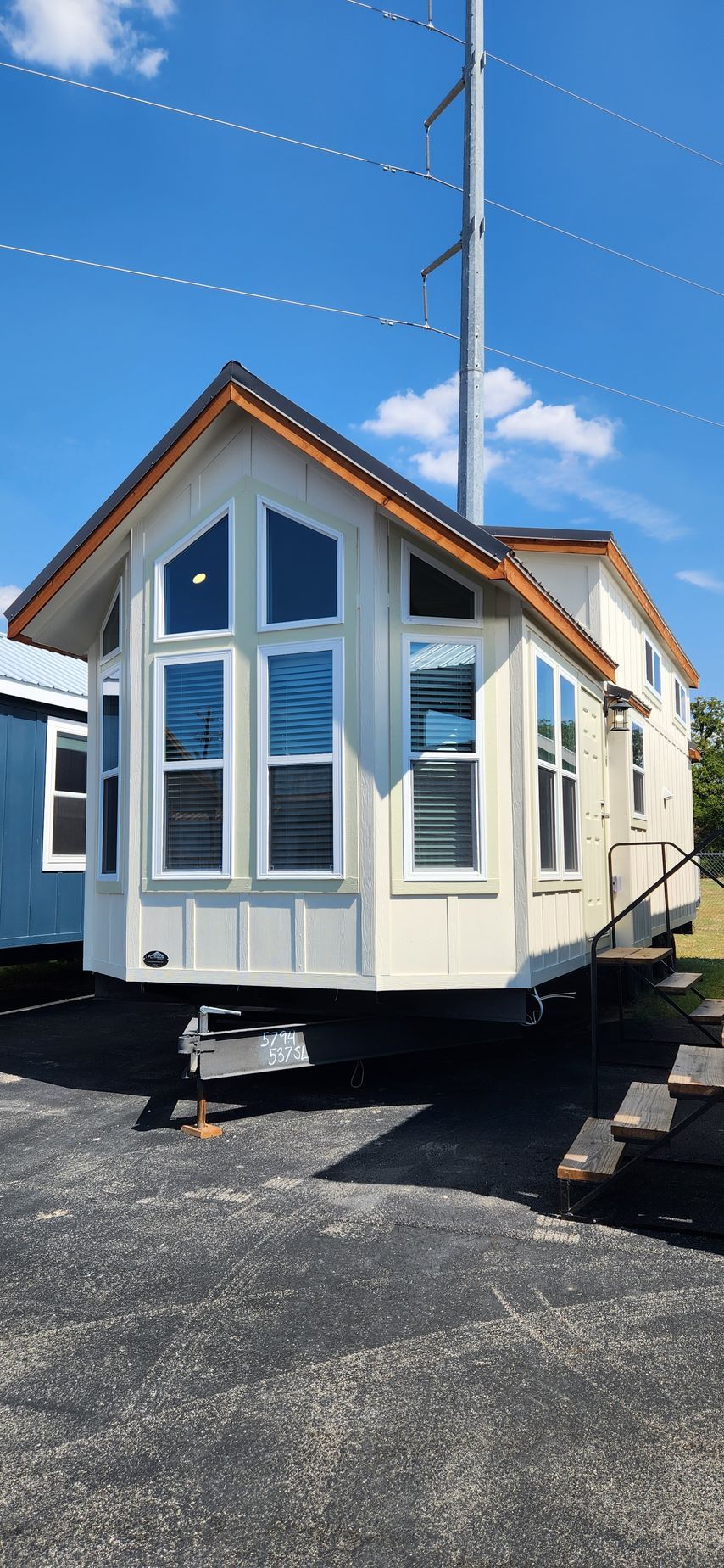 Tiny house on wheels, white siding, tall windows, angled roof, parked on gravel, blue sky.