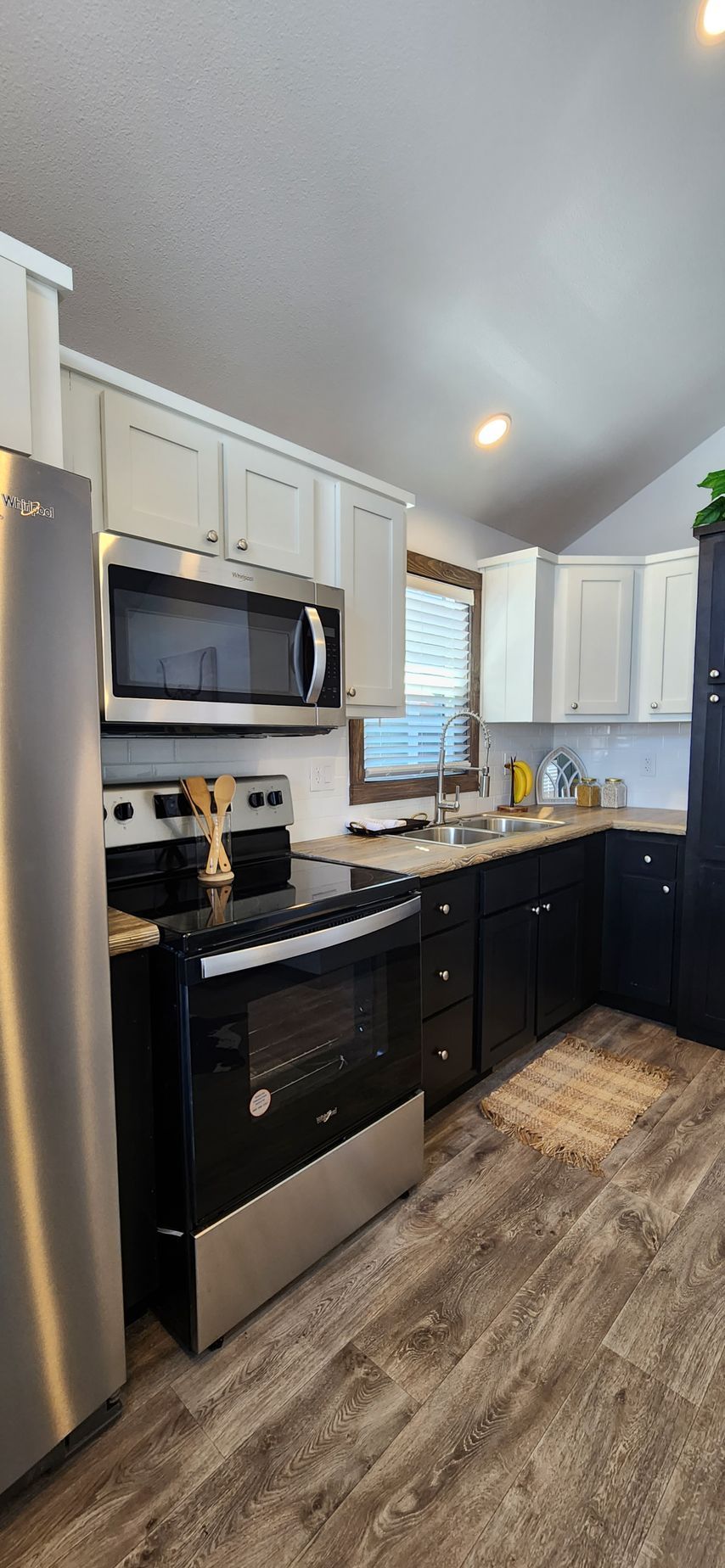 Kitchen with white and black cabinets, stainless steel appliances, and wood-look flooring.