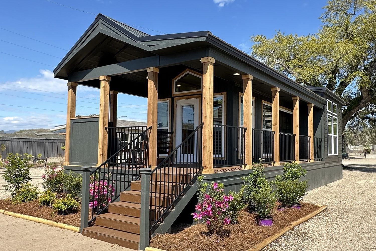 Small gray house with porch, brown pillars, steps, and landscaping.