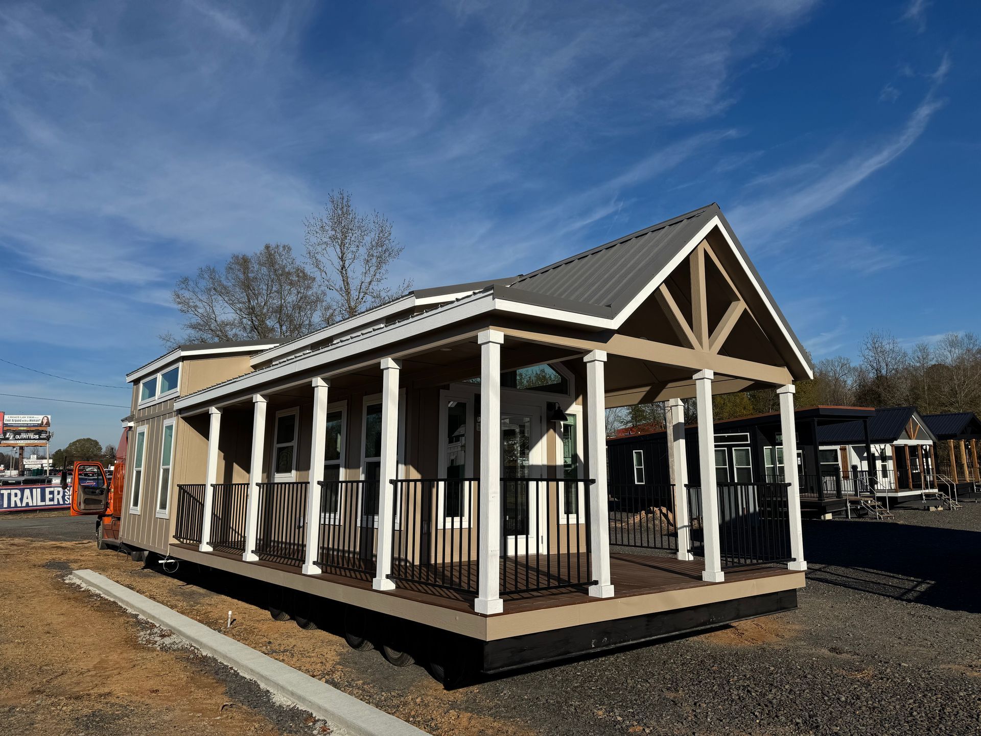 Tan tiny house with front porch and metal roof under blue sky.