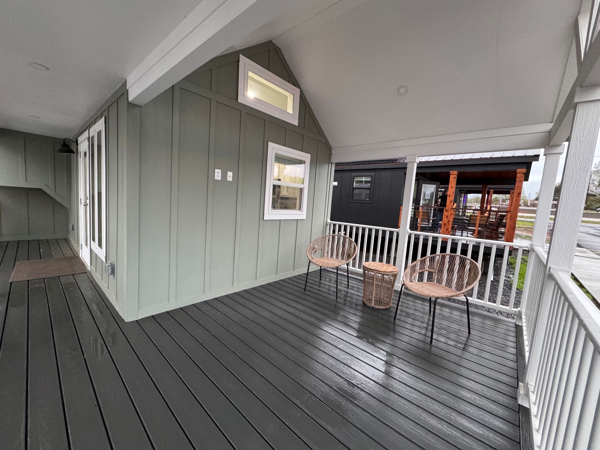 A grey porch with two wicker chairs and a small table, featuring board-and-batten siding and white railings.