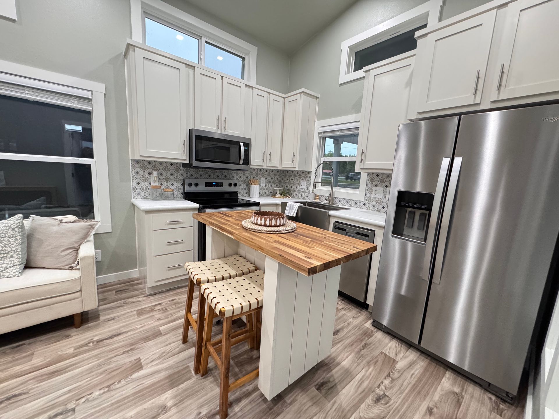 Small kitchen with white cabinets, stainless steel appliances, a wood-topped island with two stools, and light wood floors.