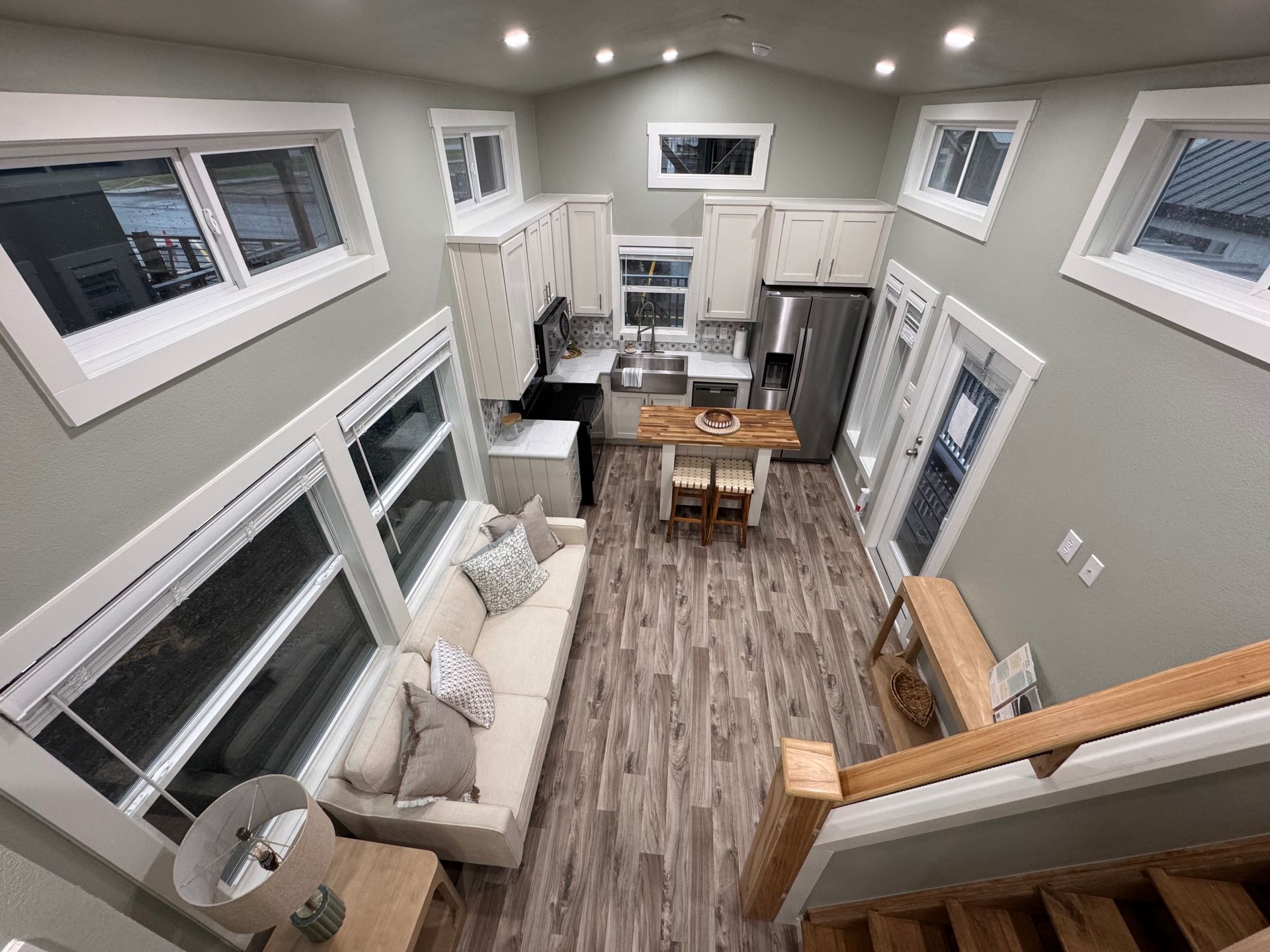 High-angle view of a tiny home living area and kitchen with a couch, dining table, and wooden staircase.