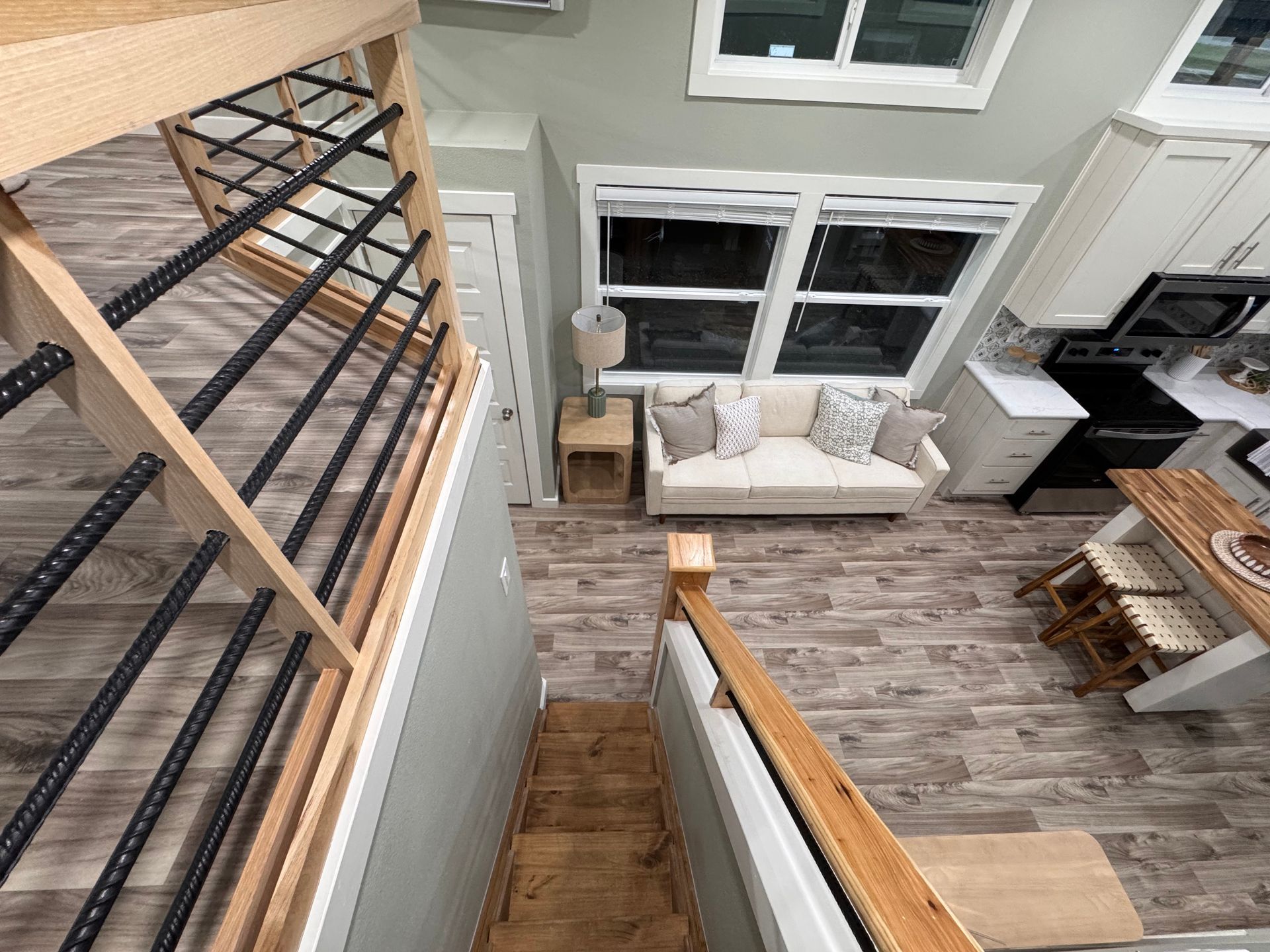 High-angle view of a living area and kitchen from a wooden staircase with black metal railings, featuring a neutral sofa.