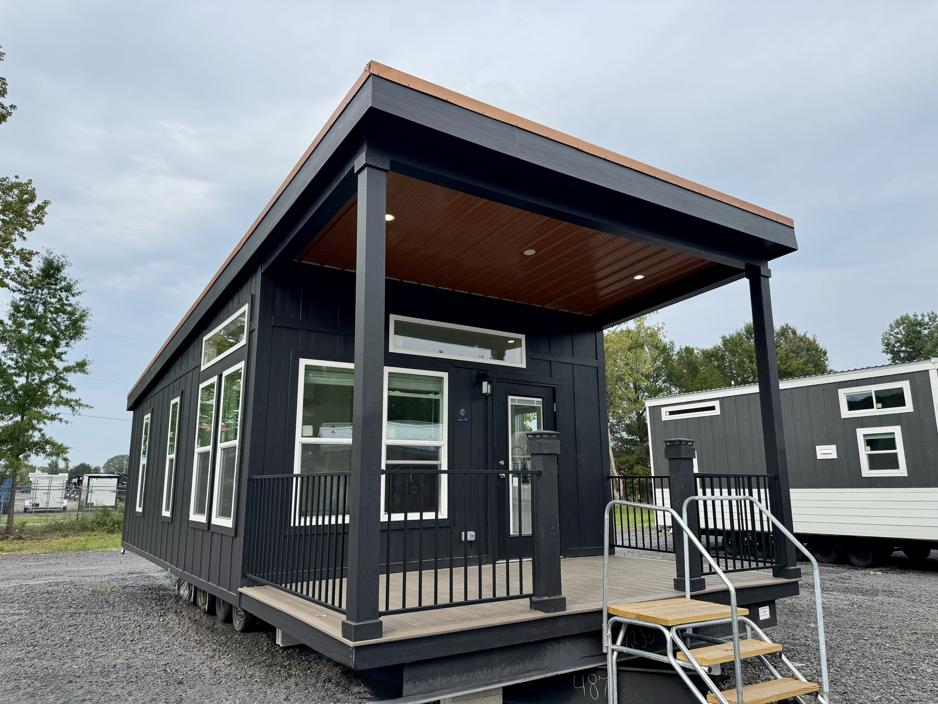 Black tiny home with porch and steps, under cloudy sky.