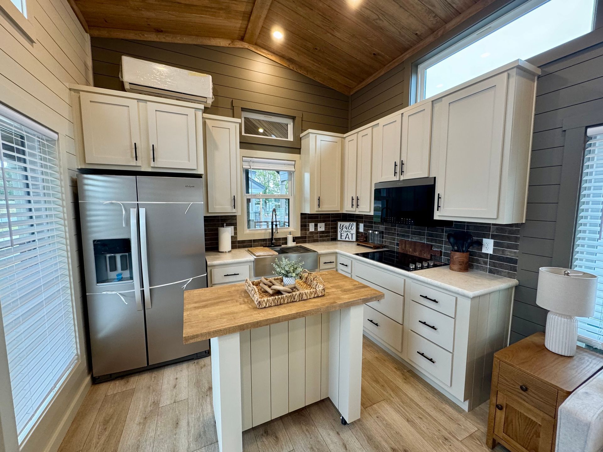 A small, modern kitchen with white cabinets, a wooden island, stainless steel refrigerator, and wood-paneled ceiling.im 