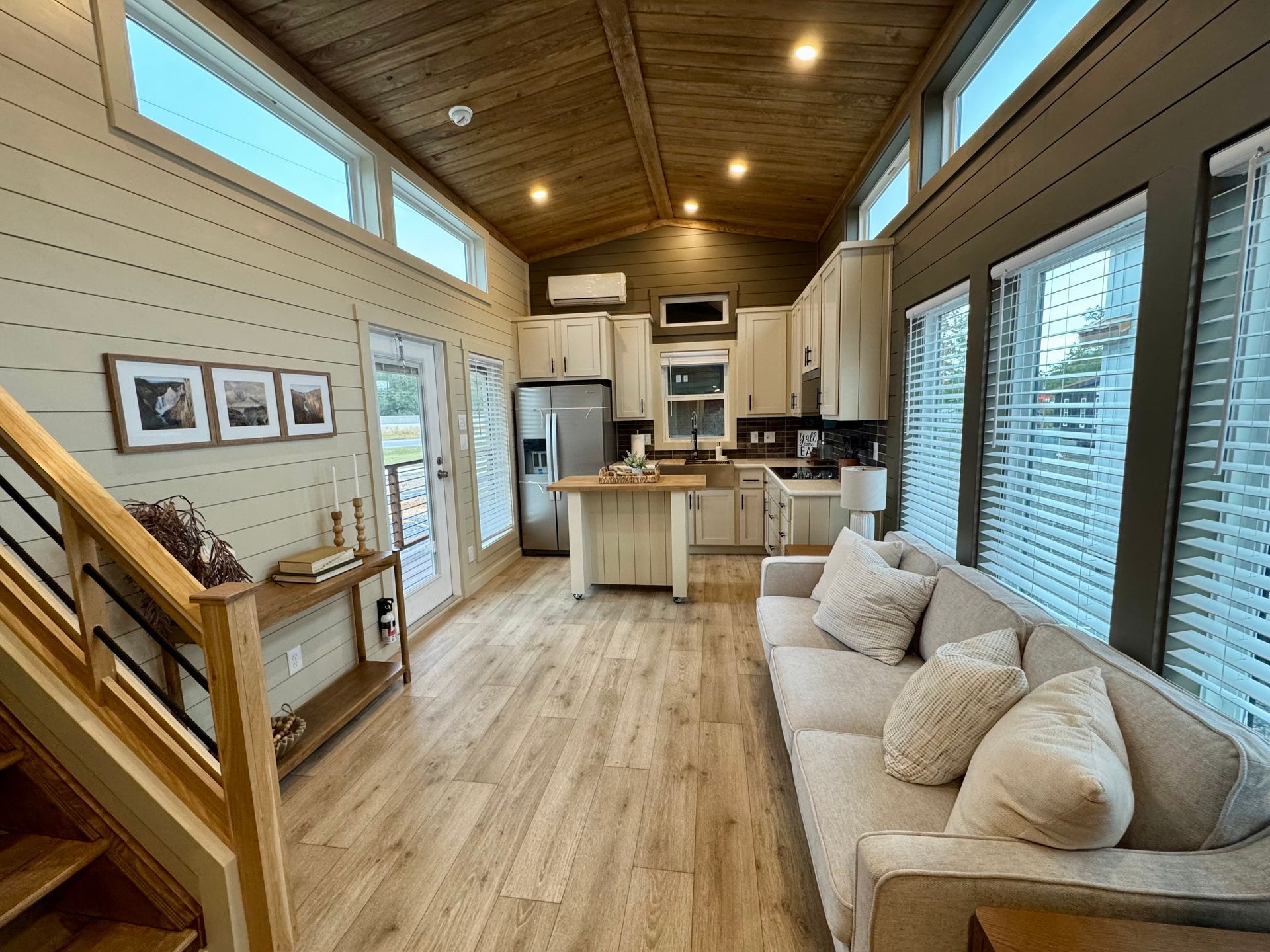 Interior view of a modern tiny home with a living area featuring a sofa, wooden floors, and an open kitchen.