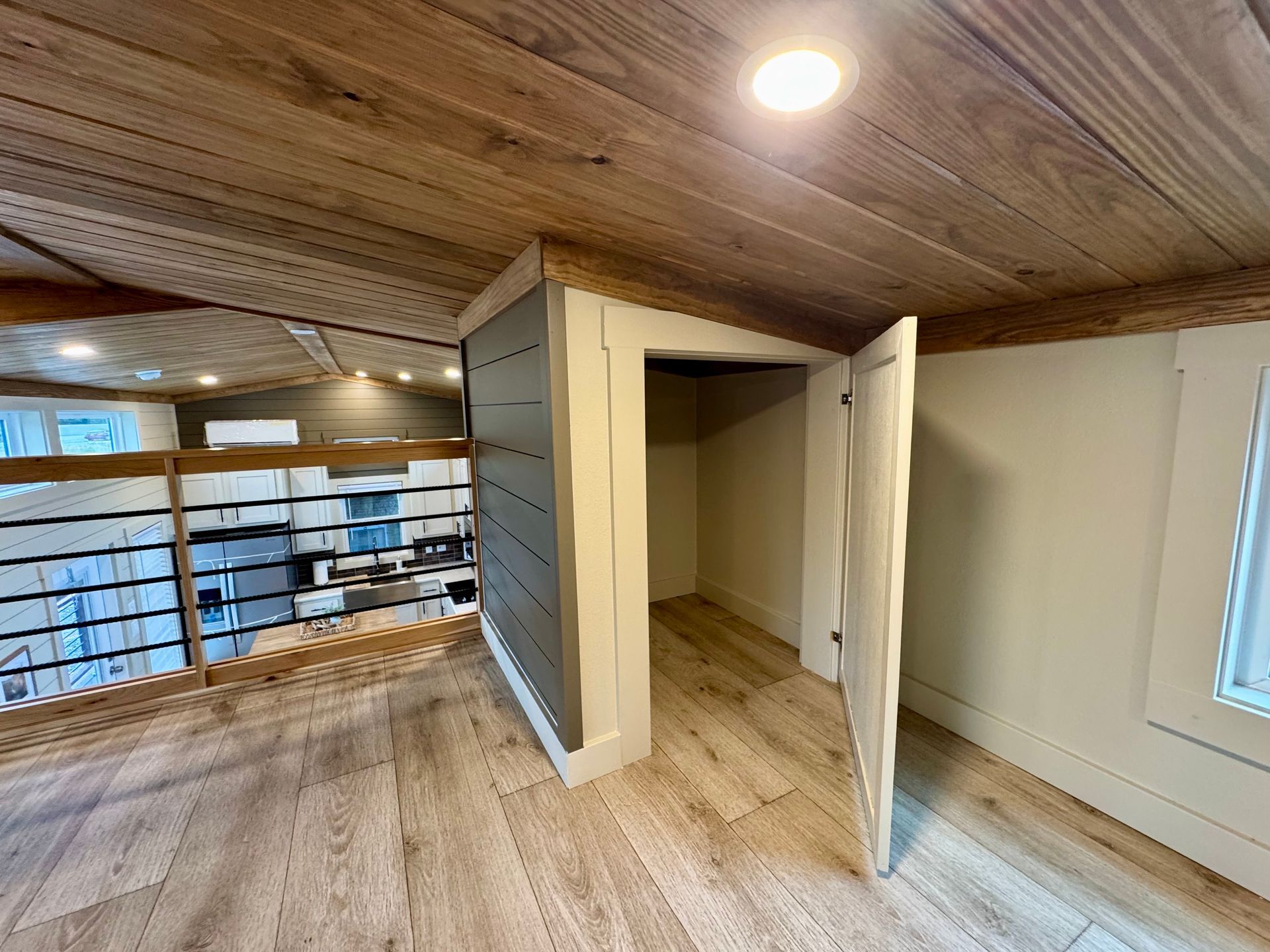 An open doorway leads into a small closet in an attic loft space with light wood floors and a wood-paneled ceiling.