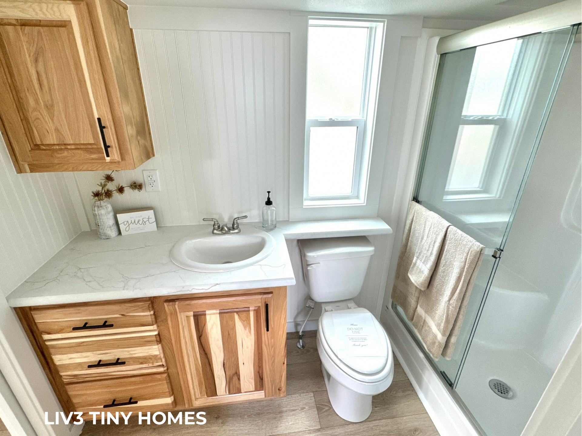A small modern bathroom featuring wooden cabinets, white countertops, a toilet, and a glass-enclosed shower.