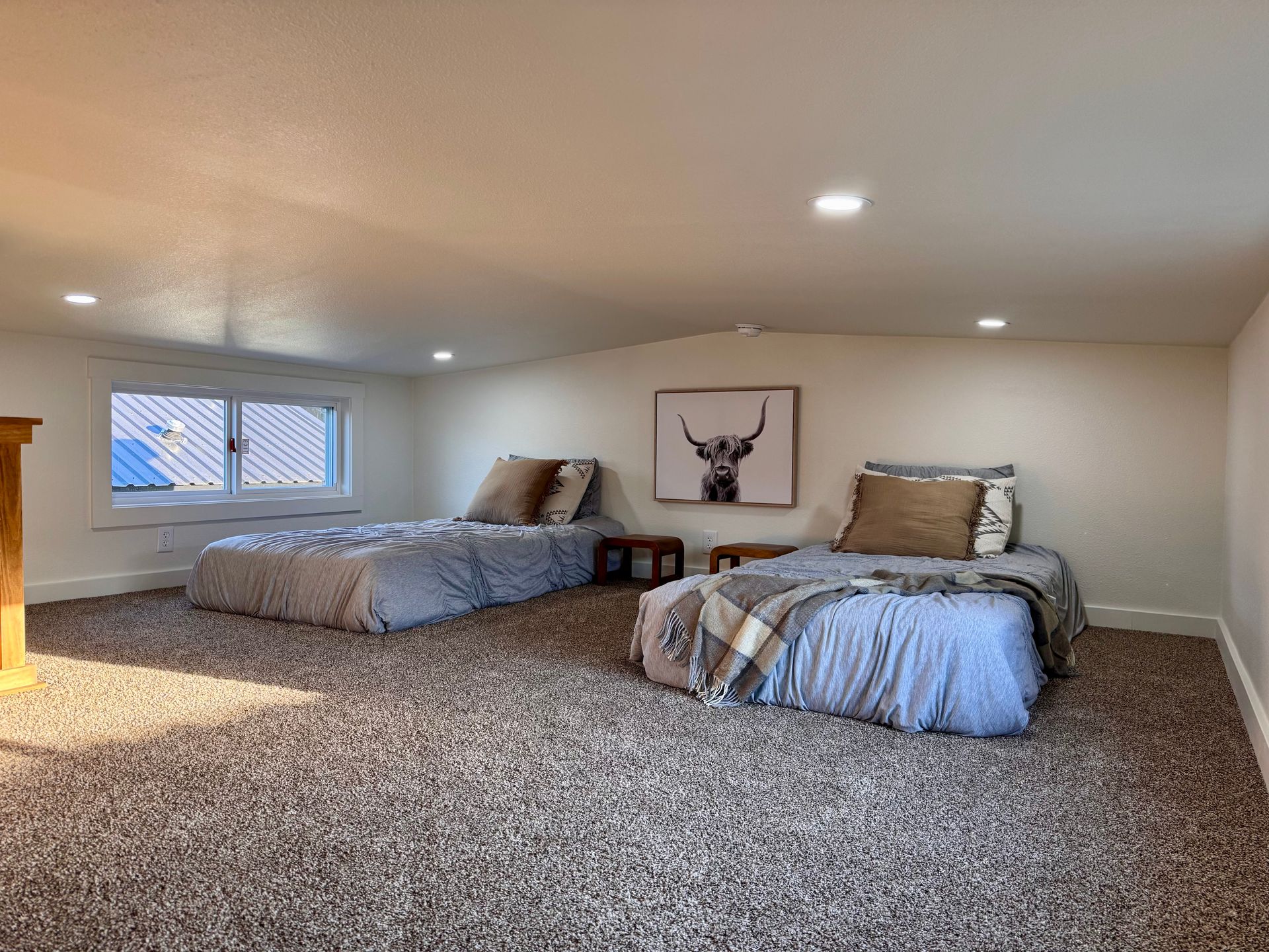 An attic bedroom with two twin beds featuring blue and white bedding, grey carpet, and a framed highland cow print.