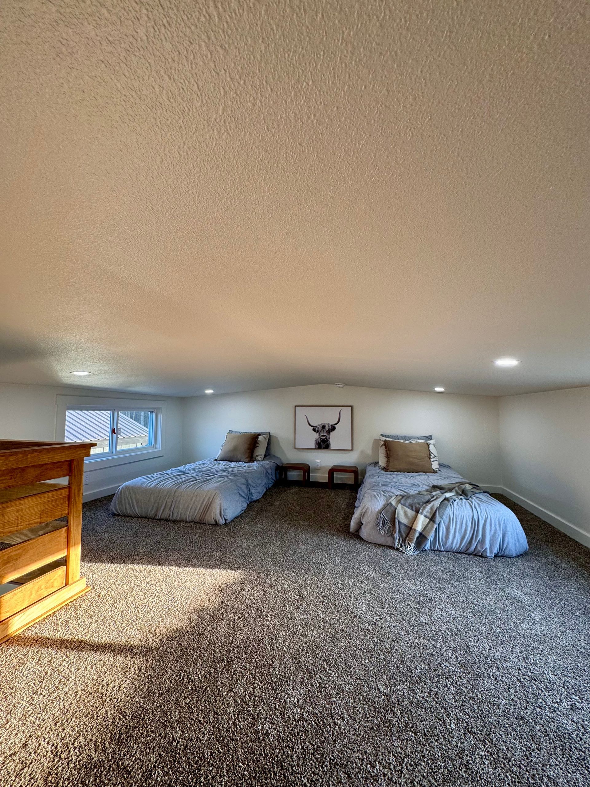 An attic bedroom with two twin beds, dark carpet, a slanted textured ceiling, and a framed deer print on the back wall.