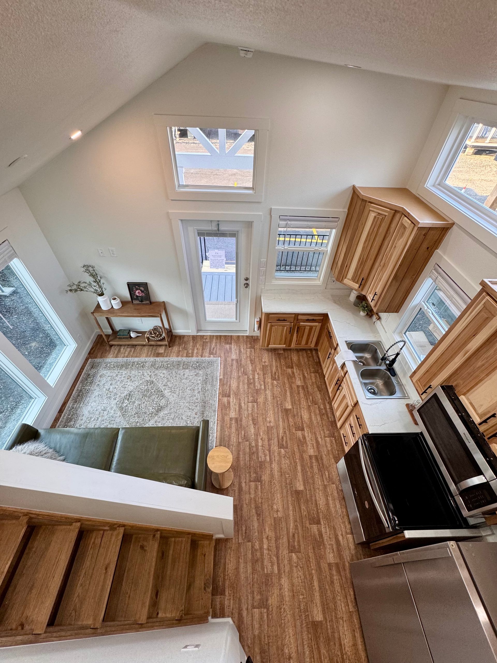 High-angle view of a tiny home living area and kitchen with wood floors, light wood cabinetry, and a green sofa.