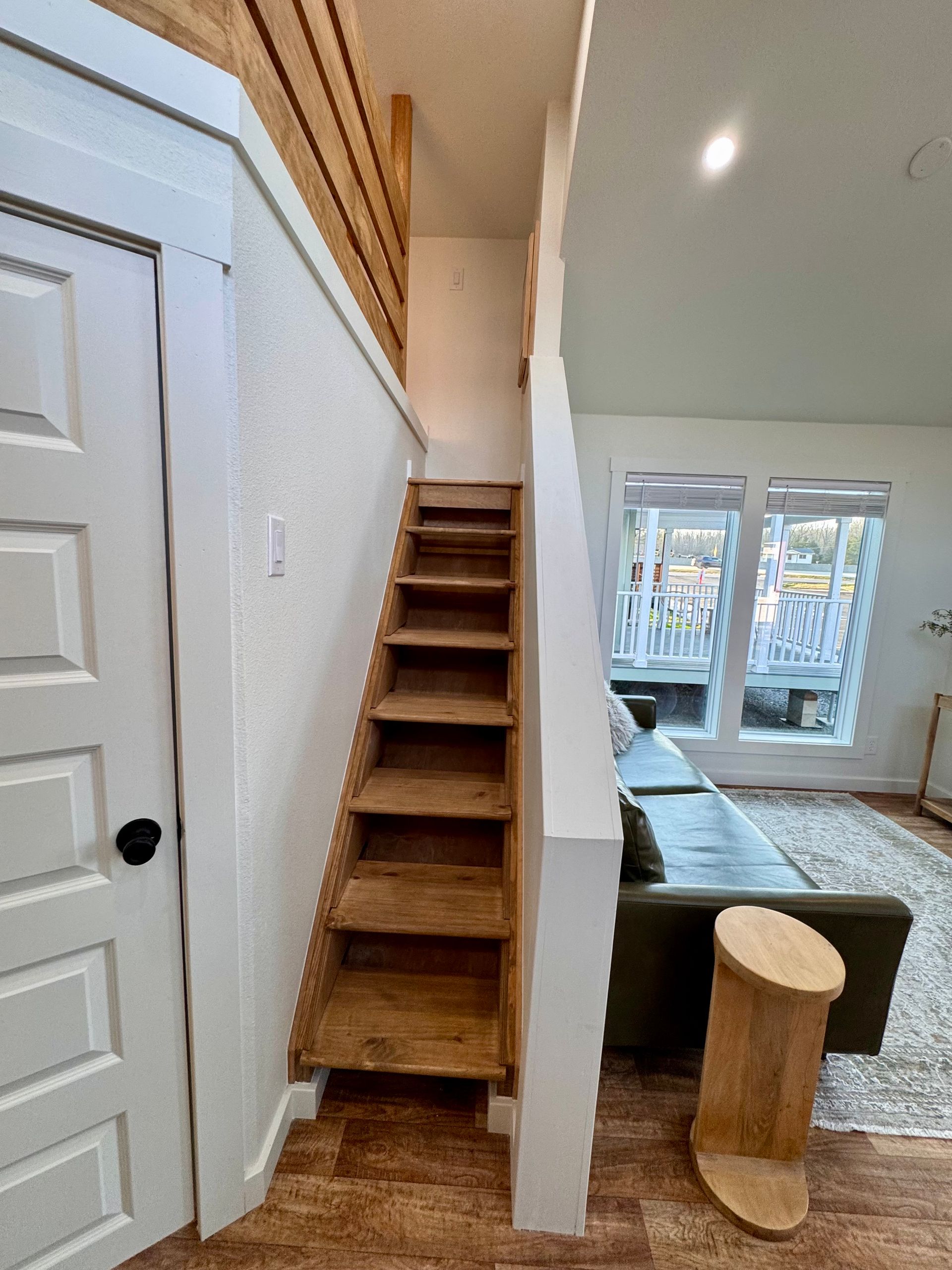 Wooden staircase leading to a loft, positioned next to a white door and a living area with a sofa.