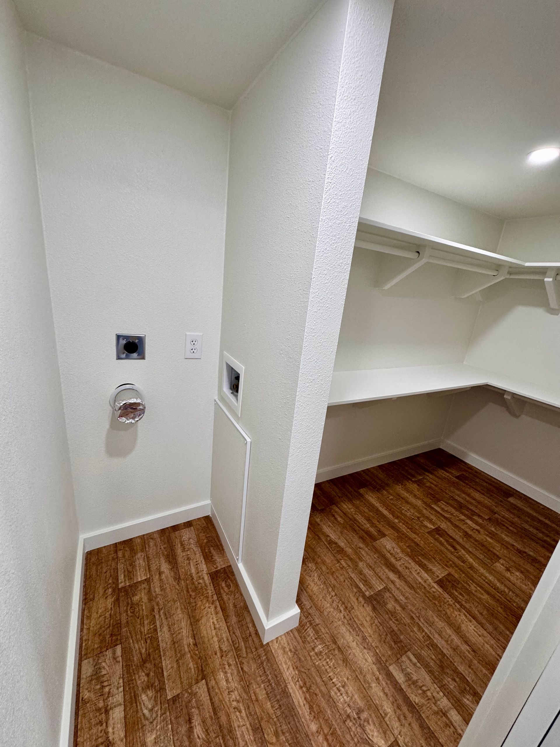 A small room with wood-look flooring featuring a laundry hookup station on the left and a walk-in closet on the right.