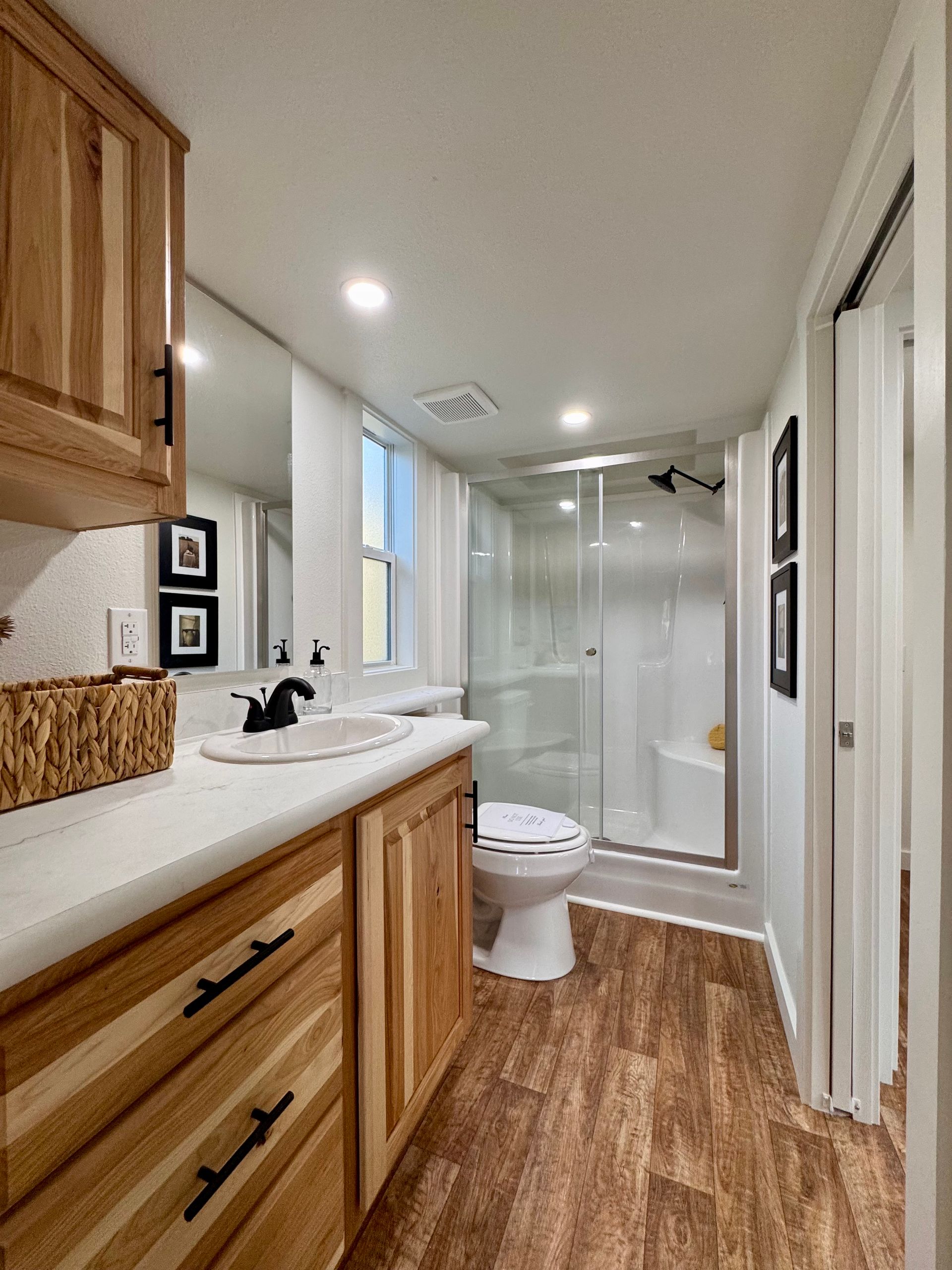 A modern bathroom featuring wood cabinetry, a white vanity with a bowl sink, a glass-enclosed shower, and wood-look flooring.