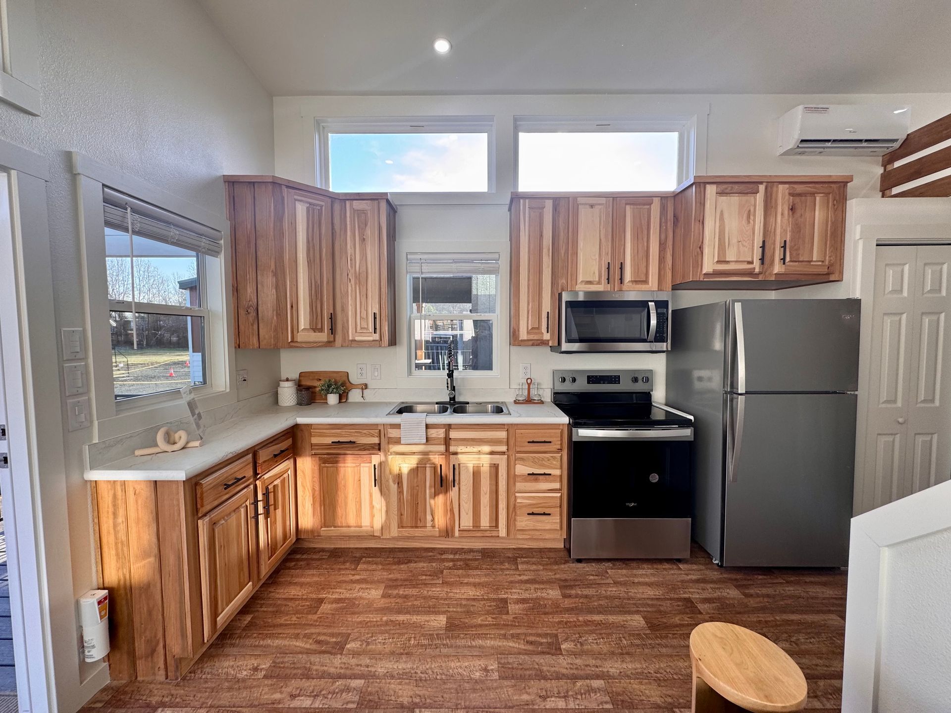 A kitchen with light wood cabinets, stainless steel appliances, white countertops, and wood-patterned flooring.