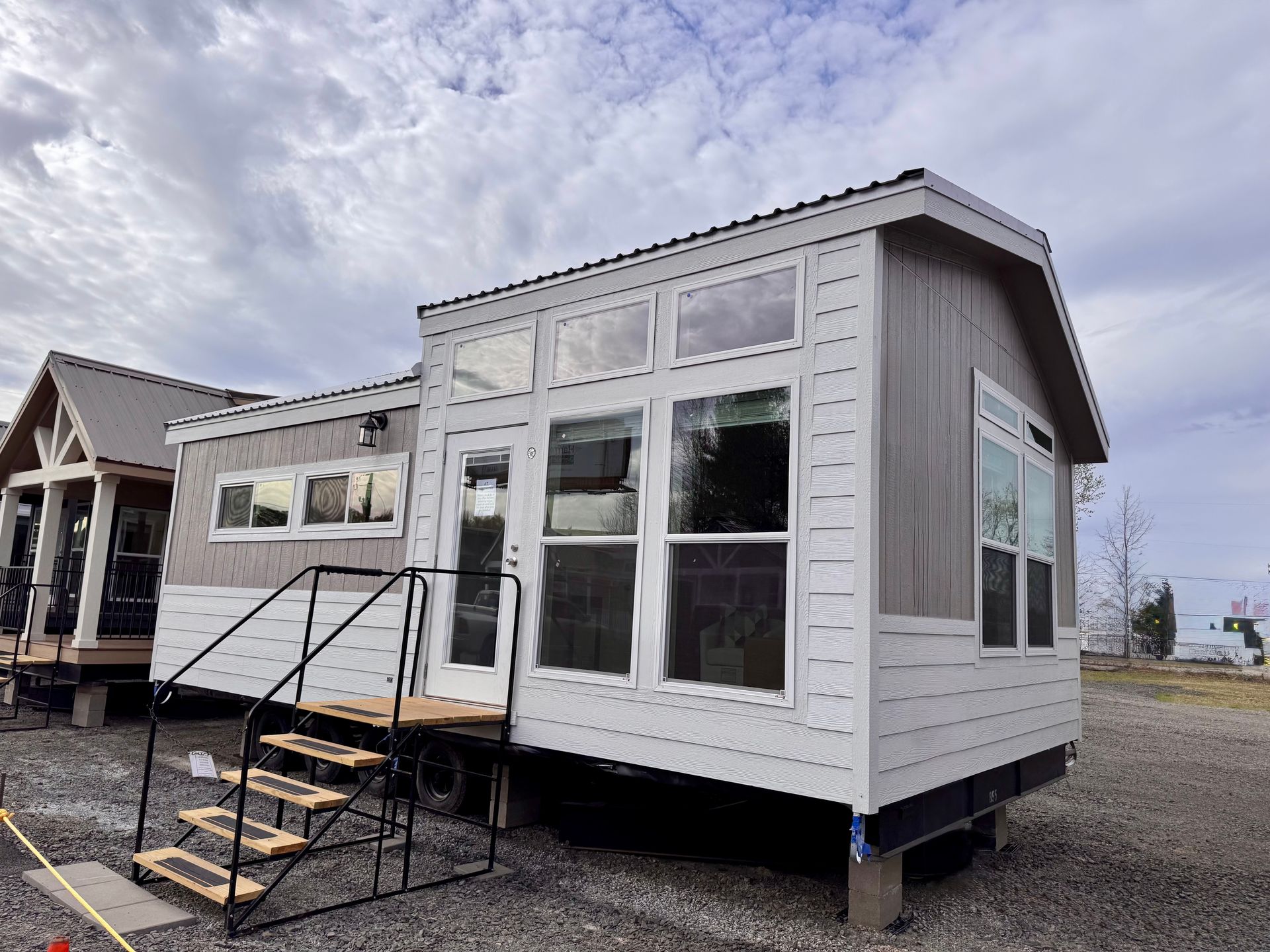 Tiny house with light gray siding, large windows, and steps leading to the door, under a cloudy sky.