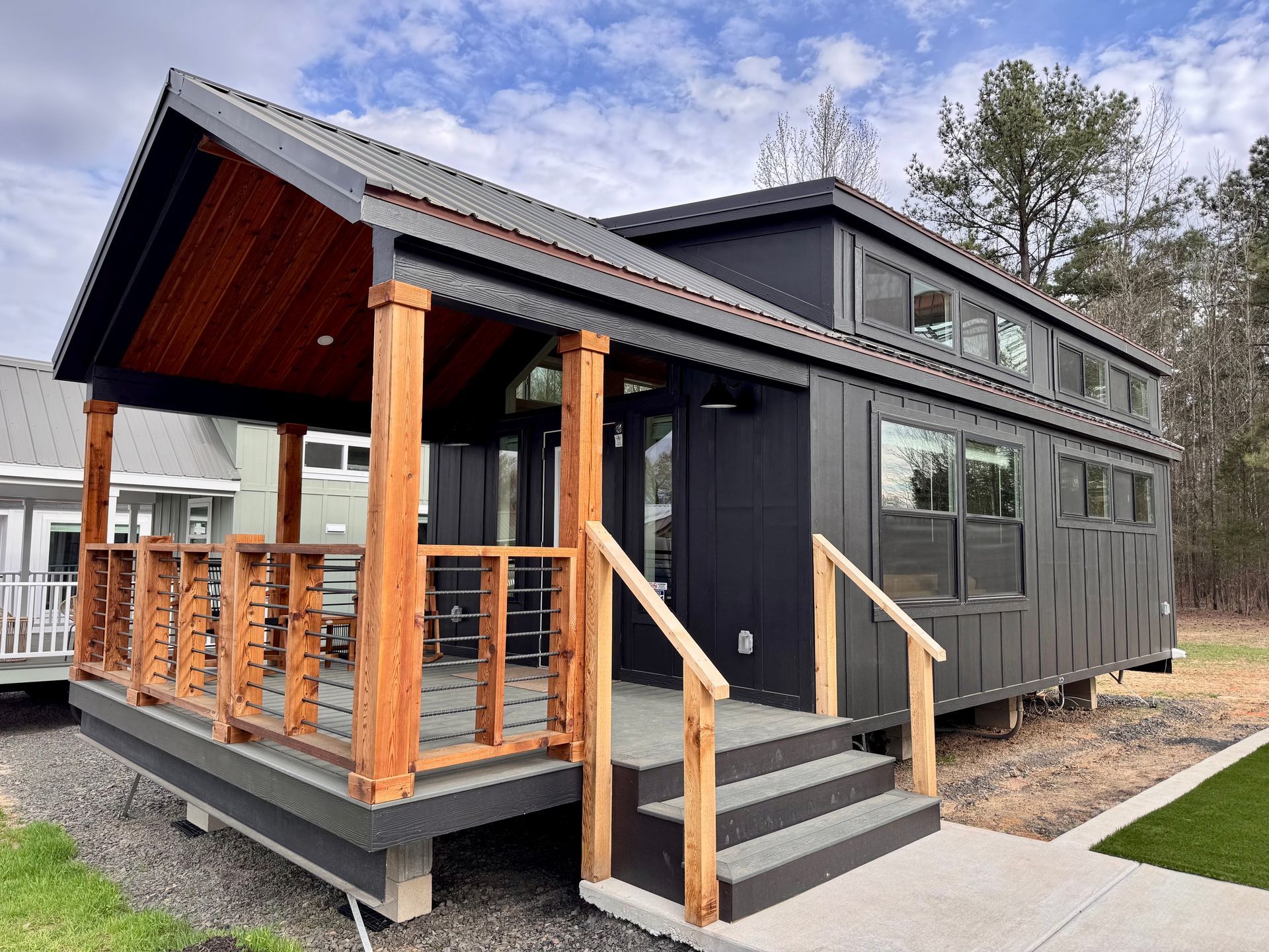 Tiny house on a foundation with a porch. Dark gray exterior, wooden accents, and a low set of stairs.