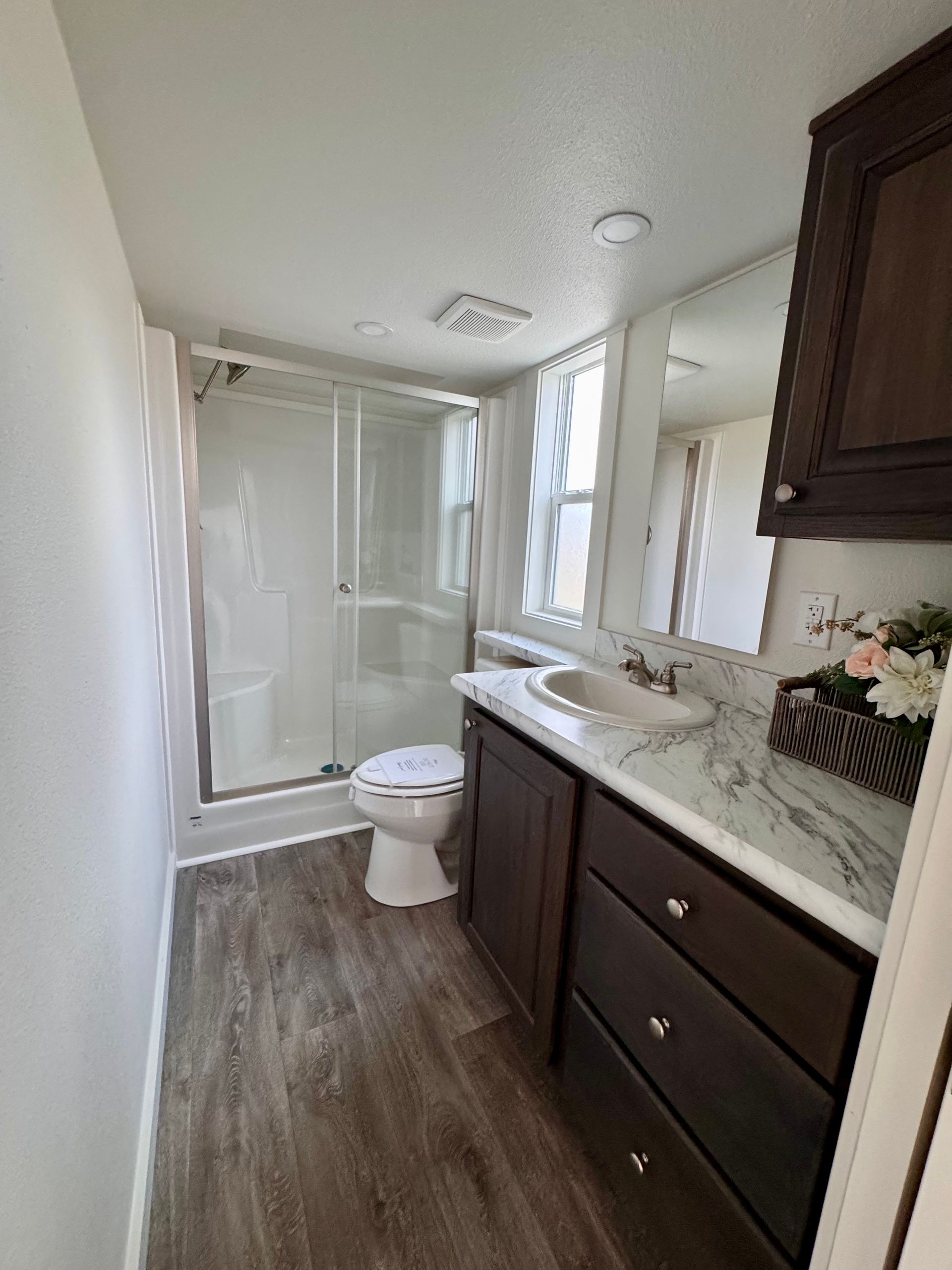 A modern bathroom featuring a glass shower, toilet, and vanity with a dark wood cabinet and marble countertop.