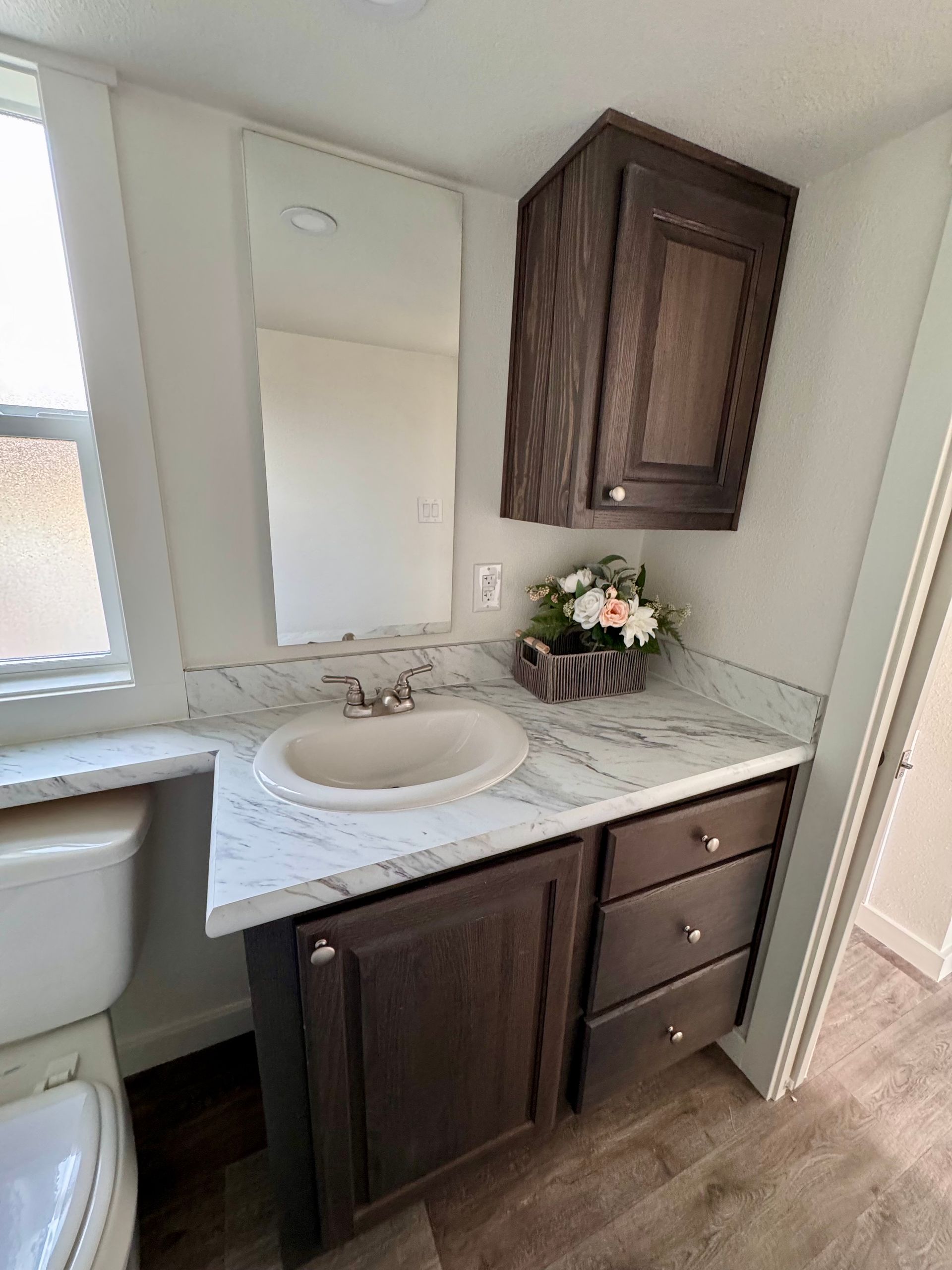 A bathroom vanity with dark wood cabinets, white marble-patterned countertop, a sink, and a matching wall-mounted cabinet.