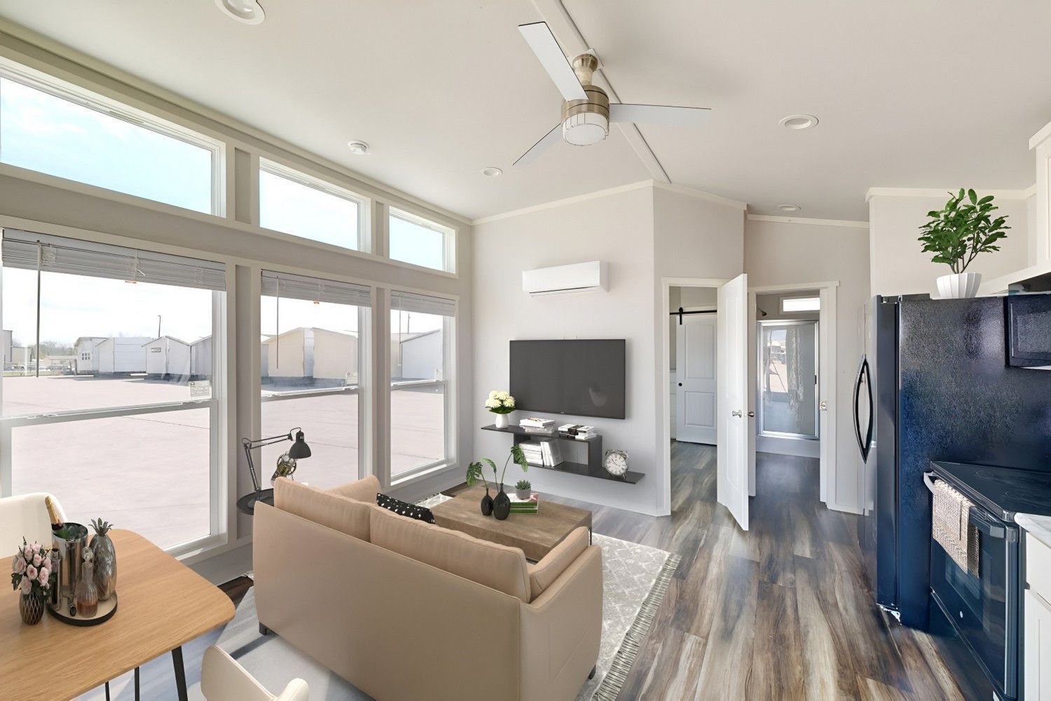 Bright living room with large windows, sofa, TV, and kitchen appliances.