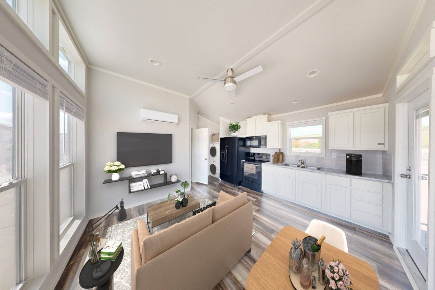 Interior of a modern living space with a kitchen. The room has light wood floors, large windows, and white walls.