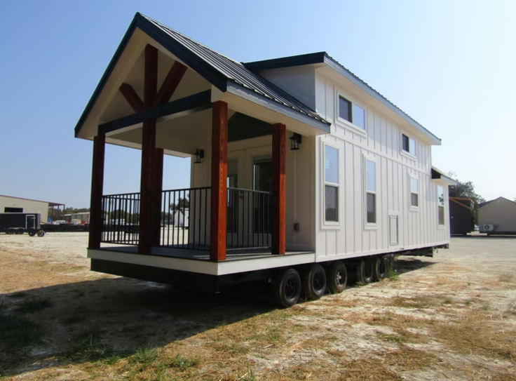 Tiny house with white siding, black roof, and porch. Located on a trailer.