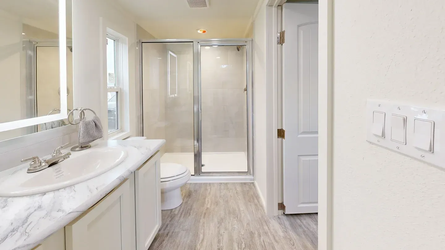 Bathroom with a marble-topped vanity, a glass shower, a toilet, and a closed white door.