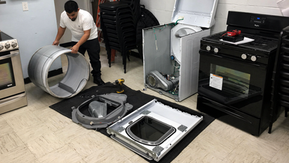 Man installing parts beside disassembled washing machine and dryer in a laundry room