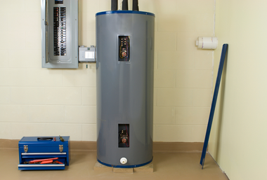 Basement utility room with a water heater, wall-mounted meter, blue toolbox, and leaning broom.